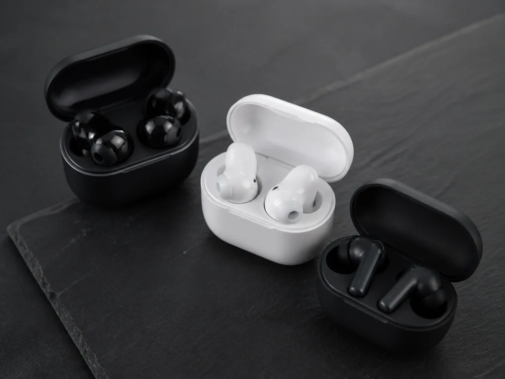 Tre par moderna true wireless earbuds i svart och vitt på mörkgrå skiffer med öppna laddningsetuin