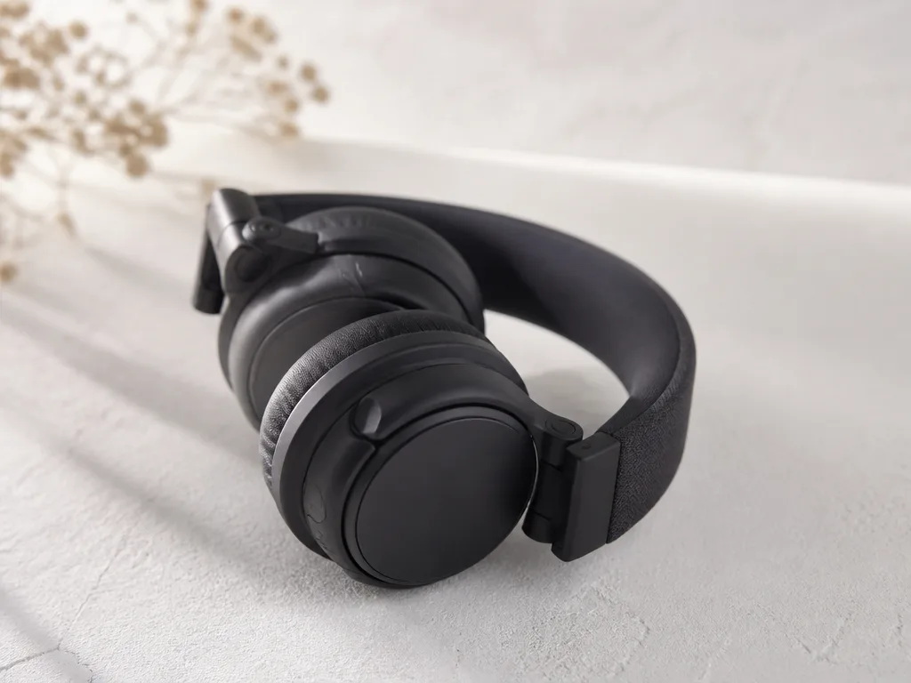 Svarta hopfällbara over ear-hörlurar med tygklädd bygel på en ljus, minimalistisk yta